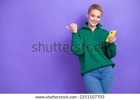 Photo of positive charming blonde short hair woman wear stylish green jumper direct finger amazon sale hold phone isolated on violet color background