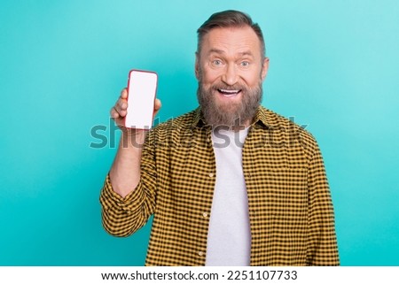 Photo of excited positive man wear plaid stylish clothes showing smartphone recommend modern mobile phone isolated on cyan color background