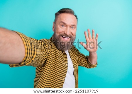 Photo of cheerful nice man wear checkered clothes demonstrate arm greetings symbol hello followers isolated on cyan color background