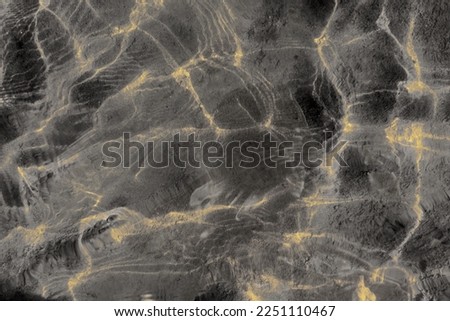Abstract photo of a transparent water surface with light reflection on the waves during the day and stones on the sandy bottom.