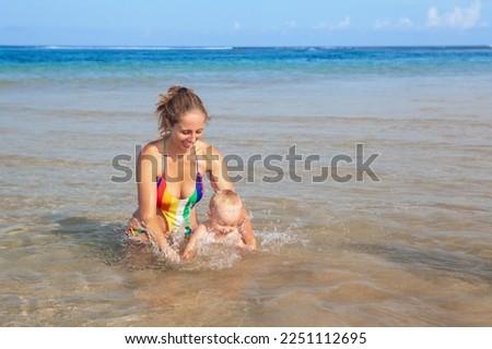 Happy kid with mother have fun on sea sand beach. Child swim and play with mother. Travel lifestyle, swimming activities in family summer camp. Vacations on tropical island.
