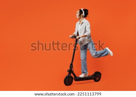 Full body young happy fun woman of African American ethnicity she wears grey shirt headband riding e-scooter look aside isolated on plain orange background studio portrait. People lifestyle concept Royalty-Free Stock Photo #2251113799