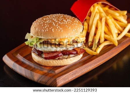 Delicious hamburger with fried egg, bacon, cheese and salad. Accompanied by french fries.