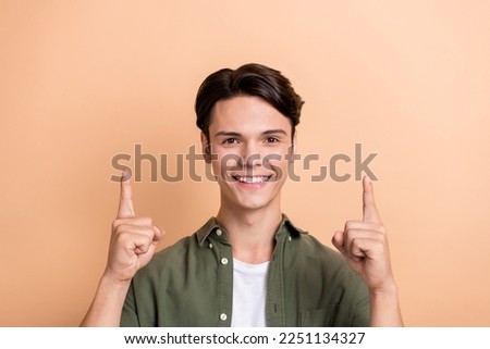 Portrait of friendly candid person beaming smile direct fingers up empty space isolated on beige color background