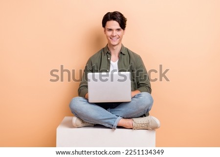 Full length cadre of young optimistic man sitting platform cube use laptop browsing information online education isolated on beige color background Royalty-Free Stock Photo #2251134349