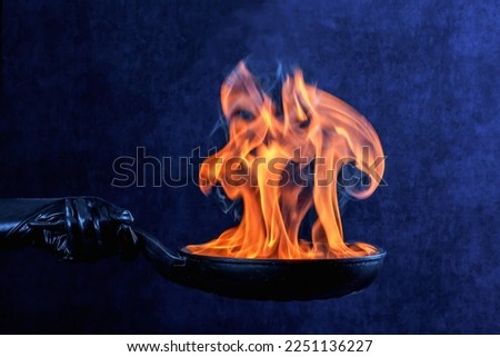 A flame in a frying pan in the hands of a woman in black gloves.