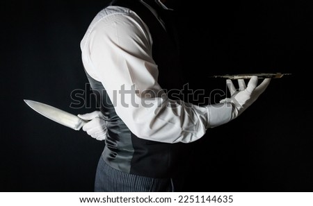 Butler or Waiter With Serving Tray and Holding Sharp Knife Behind Back. Concept of Butler Did It. Classic Murder Mystery. Royalty-Free Stock Photo #2251144635