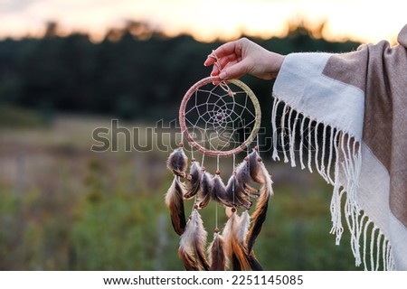 Woman with poncho holding dreamcatcher during sunrise. Spirituality and harmony between people and nature Royalty-Free Stock Photo #2251145085