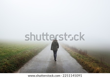 Lonely woman walks on empty road in fog. Journey to unknown place. Solitude female person walking outdoors Royalty-Free Stock Photo #2251145091