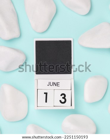 White wooden calendar with the date june 13 on a blue background with white pebbles