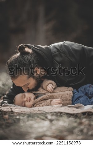New born family photo shoot in the fall by the woods. Father kissing sleeping baby