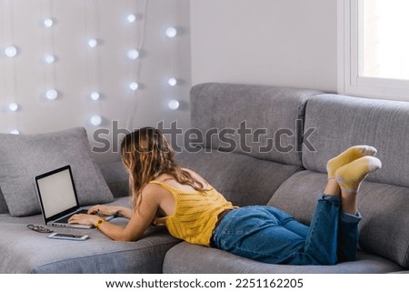 Blonde woman lying on sofa working with laptop at home
