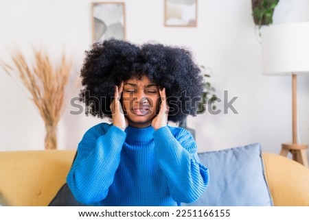 Cheerful black woman sitting on sofa and headache