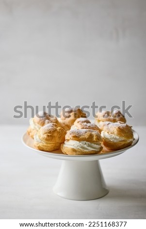 plate of cream puffs decorated with powdered sugar on light grey background