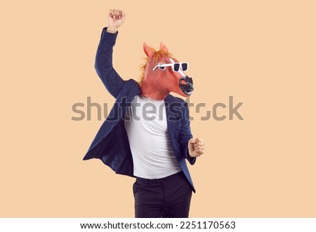 Portrait of strange man wearing T shirt, suit jacket, funny horse mask and sunglasses having fun and dancing isolated on beige background. Fun, party, humor concept Royalty-Free Stock Photo #2251170563