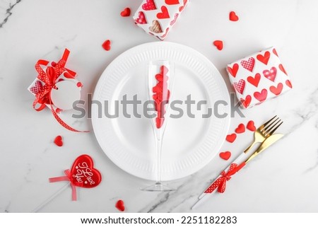 Valentines day dinner background with gifts, wine glass with red hearts, plate, cutlery on white marble. Romantic holiday table setting. Festive table setting on marble background. Top view, flat lay