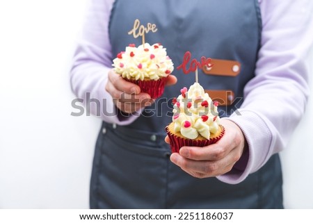 Woman waitress with two cupcakes decorated with red hearts topping and wooden sign with LOVE letters. Valentine's Day and Mother's Day concept. White background.