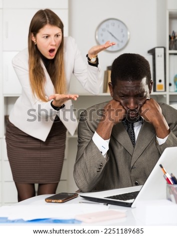 Portrait of young stressed businessman in office with dissatisfied female chief behind Royalty-Free Stock Photo #2251189685