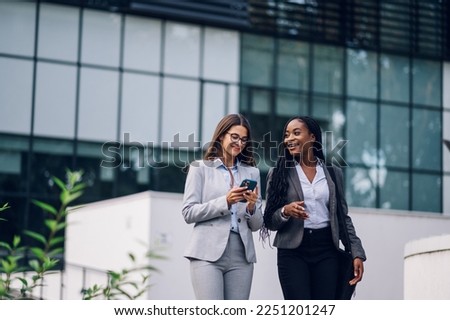 Team of multiracial successful business women on their way to the office talking about strategy and using a smartphone. Diverse women walking outside with buildings in the background. Teamwork.