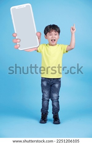 Photo of a little Asian cute child, holding a big giant smart phone to show the screen, isolated on background. Concept of promoting an application. 