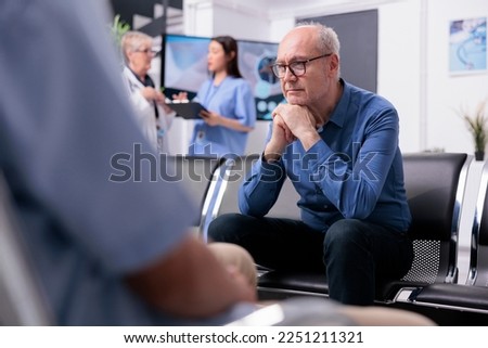 Stressed tired senior patient sitting on chair in hospital lobby while waiting for specialist doctor to start medical examination during checkup visit consultation. Health care service and concept Royalty-Free Stock Photo #2251211321
