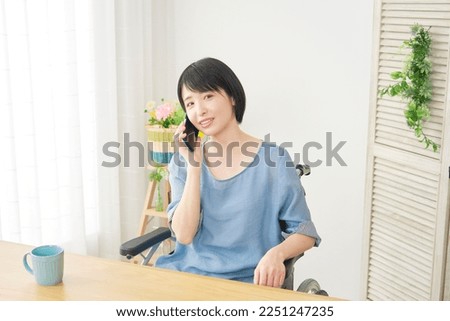 Asian woman on the wheelchair calling with the smartphone at home