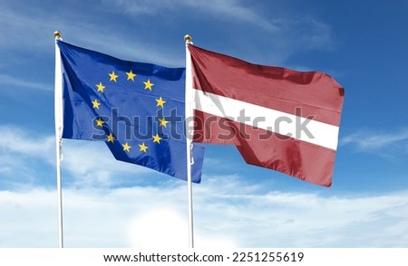 Latvian flag and European Union flag on cloudy sky. waving in the sky