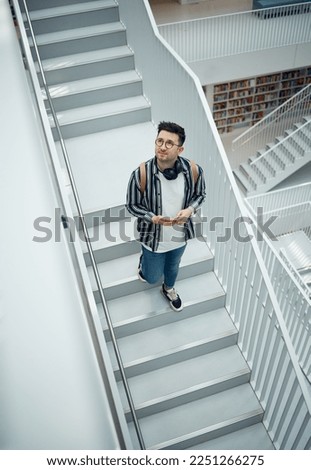 Library, staircase and student man walking in a education, learning and school research building. College learning, study and bookshelf of person walking down stairs looking at books for information