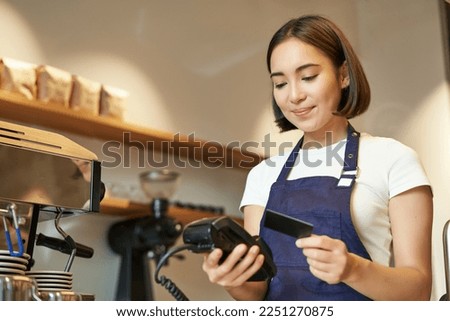 Cute asian girl, barista in cafe processing contactless payment, insert credit card into POS terminal, taking order in cofee shop.