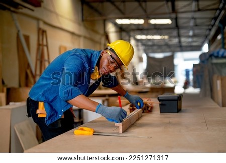 African American carpenter man use pencil to mark on timber during work with in wood factory workplace. Royalty-Free Stock Photo #2251271317