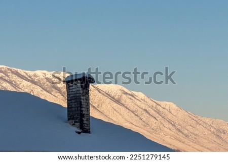 Artistic and minimalist picture of a stone chimney on a roof in winter, under the snow, with the Mali i Gjerë mountains in the background. Gjirokastër (Gjorikaster), Albania.