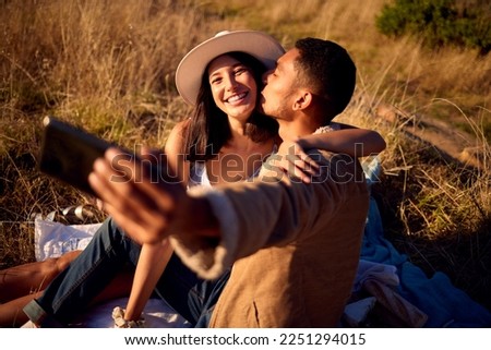 Couple kiss in selfie with hug, outdoor and picnic in nature, love with smartphone, technology and happy together. Phone for photography, man and woman smile in picture with travel and summer date