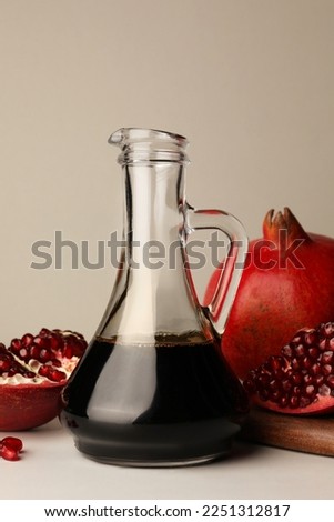 Glass jug of tasty pomegranate sauce and fresh ripe fruits on white marble table