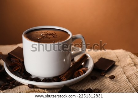 Cup of delicious hot chocolate, spices and coffee beans on table. Space for text