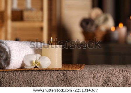 Spa composition with candle, orchid flower and rolled towel on massage table in wellness center, space for text Royalty-Free Stock Photo #2251314369