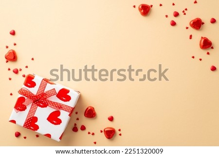 Saint Valentine's Day concept. Top view photo of white giftbox with red ribbon bow heart shaped candies and sprinkles on isolated light beige background with copyspace