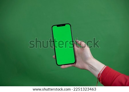 women's hand shows mobile smartphone with green screen in vertical position isolated on green background - mockup template and clipping path