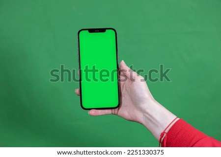 women's hand shows mobile smartphone with green screen in vertical position isolated on green background 