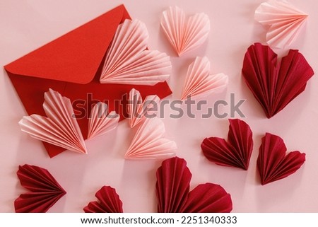 Valentines day flat lay. Stylish red envelope with pink and red hearts composition on pink paper background. Creative modern valentines hearts cutouts. Love letter. Happy Valentine's day