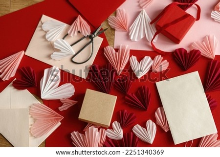 Happy Valentine's day! Stylish empty card, gift box, red and pink hearts, scissors, paper on wooden table top view. Valentine day holiday preparations. Modern creative love letter mock up