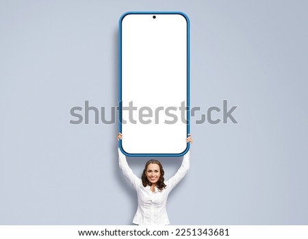 Smiling business woman, showing big cell phone, mobile smartphone. Happy businesswoman holding over head cellphone with mockup white screen, isolated over grey background. App ad concept image.