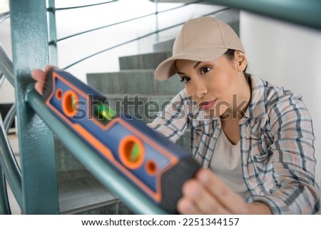female builder checking staircase railing with spirit level