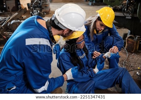 Painful accident in industrial production metalwork, African American female worker injured her hand, male engineer and colleague team helped first aid with care at manufacturing machinery factory.  Royalty-Free Stock Photo #2251347431