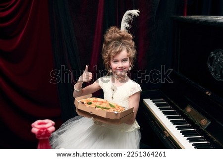 Portrait of cute little girl, child in image of medieval royal person sitting at the piano with pizza. Delicious taste. Concept of historical remake, comparison of eras, medieval fashion, childhood