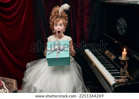 Portrait of cute little girl, child in image of medieval royal person emotionally opening presents. Surprise. Concept of historical remake, comparison of eras, medieval fashion, emotions, childhood