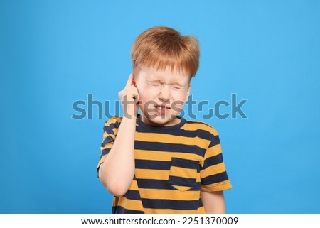 Little boy suffering from ear pain on light blue background Royalty-Free Stock Photo #2251370009