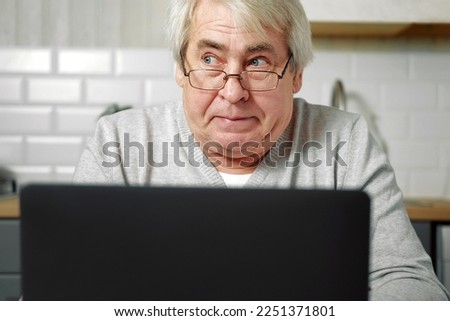 Senior grey haired man wearing glasses sitting at laptop and making fish face with lips. Comical gesture. Funny Old grandfather with playful silly facial expression grimacing fooling around