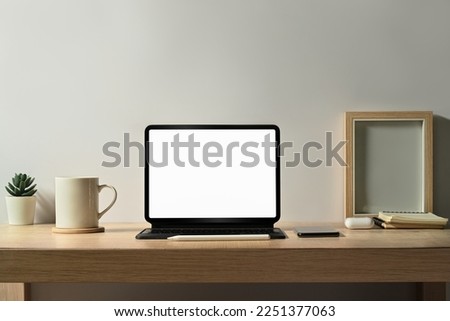 Comfortable workplace with tablet, picture frame, coffee cup and houseplant on wooden table. Blank screen for your advertise