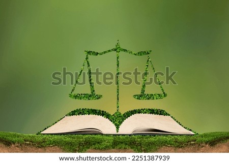 Law book and scales with green leaves on green background.