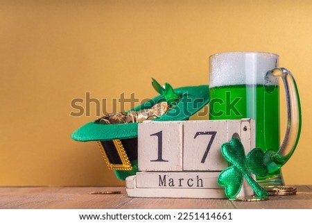 Beer glasses with leprechaun hat, shamrock clover leaves, traditional decorations for St. Patrick's Day, on gold wood background. St. Patrick's Day Ireland holiday greeting card, invitation background